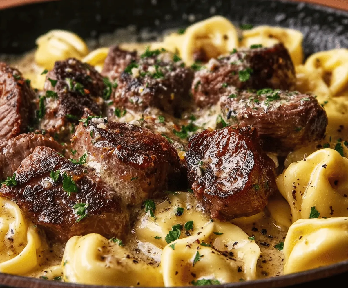 Delicious sizzling butter steak bites served alongside creamy velvety Alfredo tortellini on a white plate